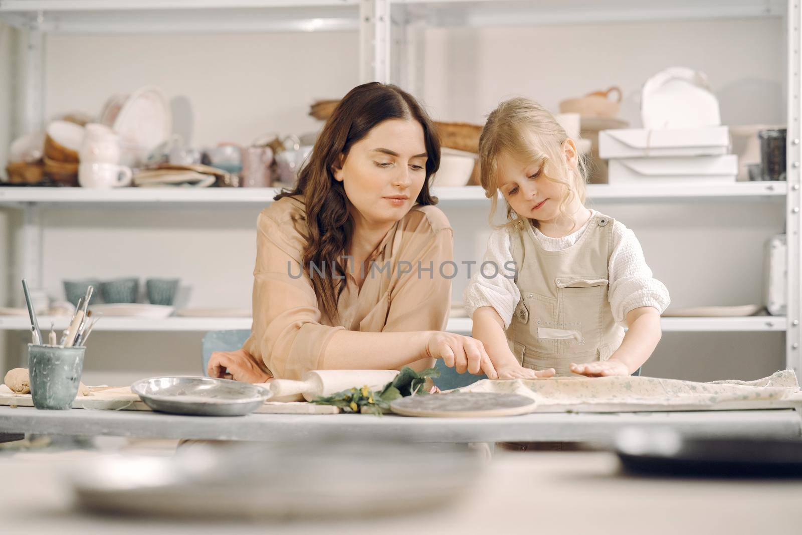Woman and girl kneading clay. Family make art product at table in pottery workshop. Mother with daughter.
