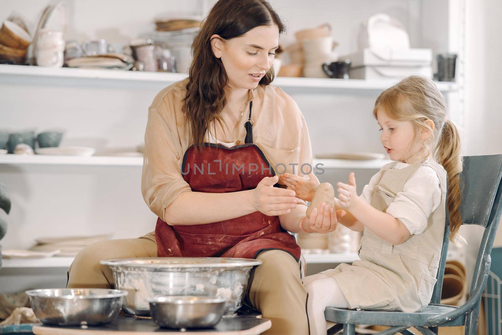 Woman and girl kneading clay. Family make art product at table in pottery workshop. Mother with daughter.