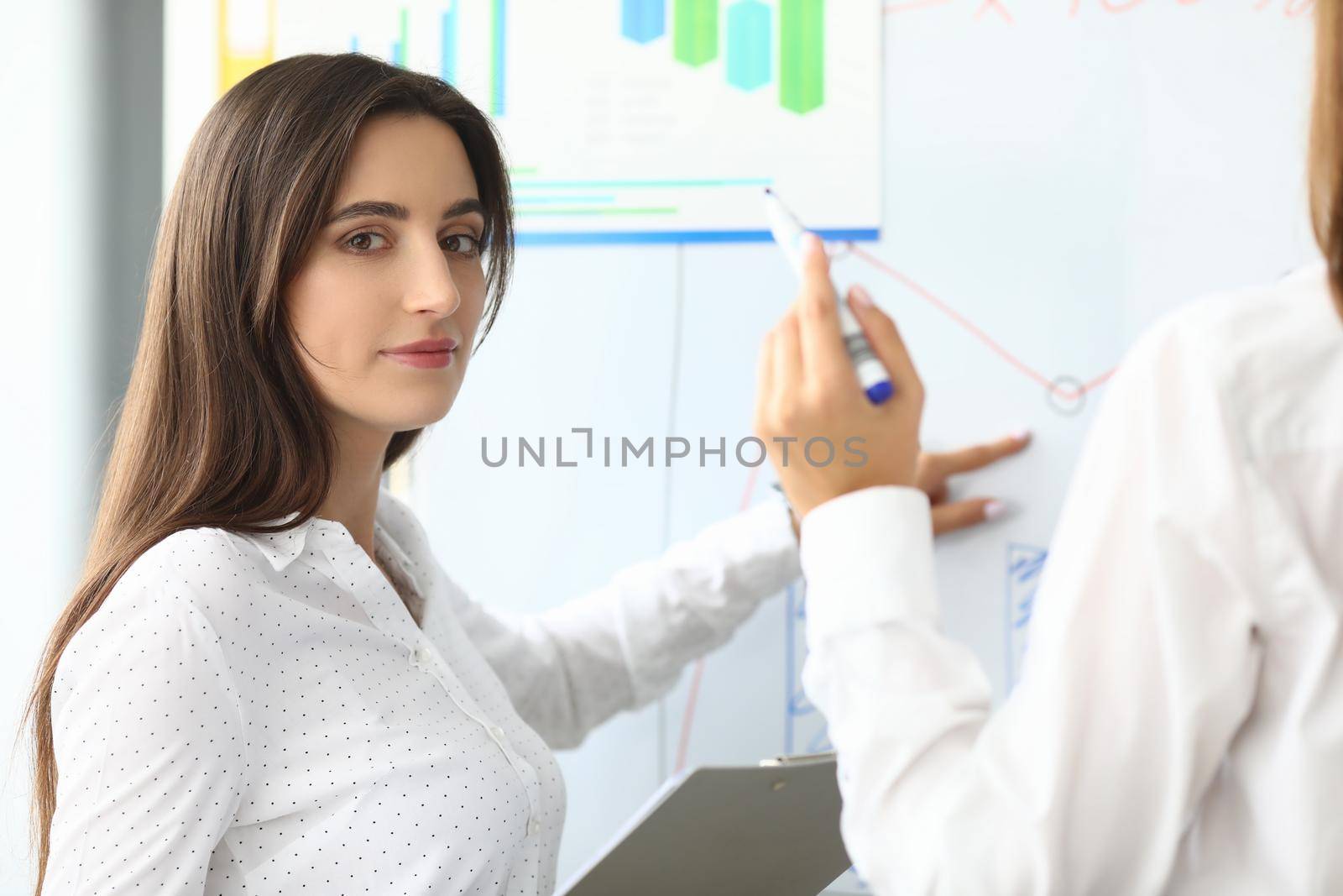 Portrait of smart businesswoman sitting in modern workplace and pointing at something on modern glass board with tender hand. Accounting office concept