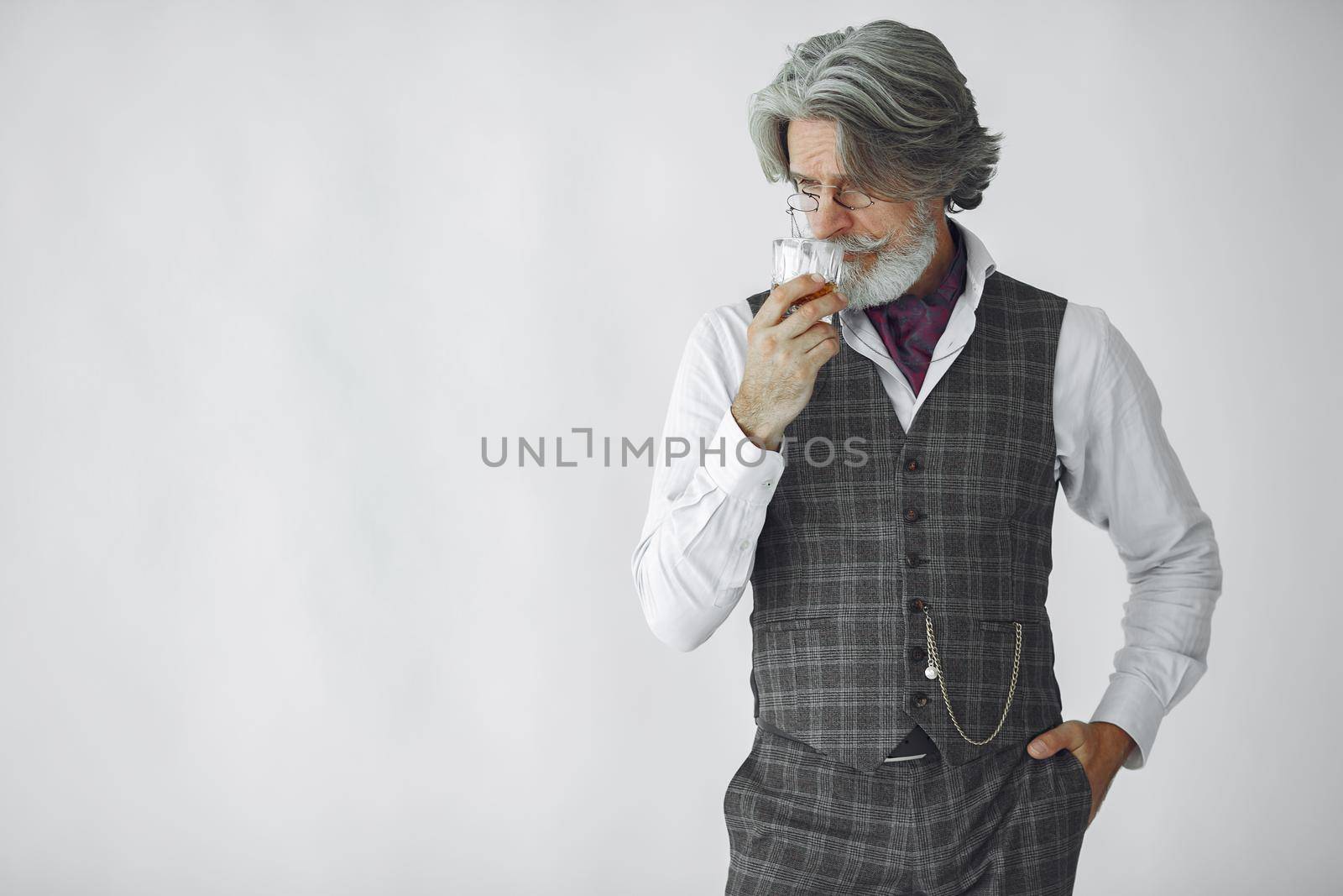 Close up portrait of grinning old-fashioned man. Elegant man in a studio. Grandfather with a glass of whiskey.