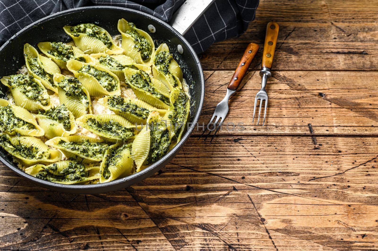 Jumbo shells pasta Conchiglioni stuffed with spinach and cheese baked with sauce in a pan. Wooden background. Top view. Copy space by Composter