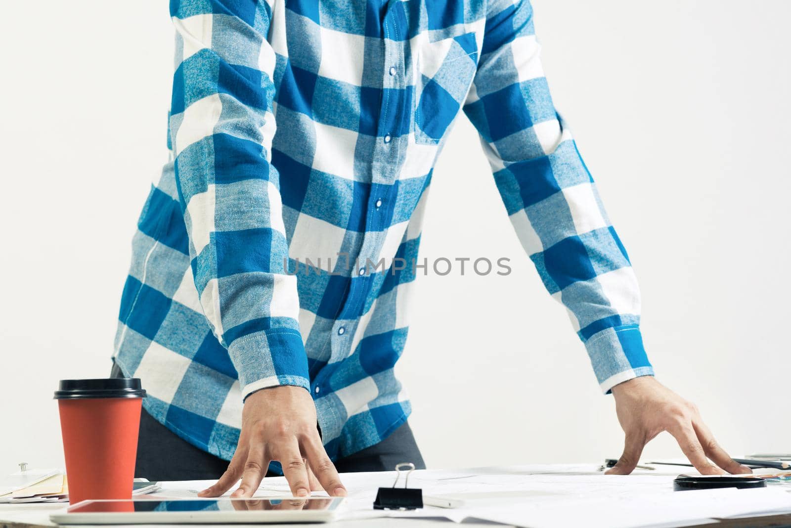 Architect standing near desk with blueprints and cup of coffee. Architecture studio concept with design project. Close up man hand lying on technical drawing. Professional building and engineering.