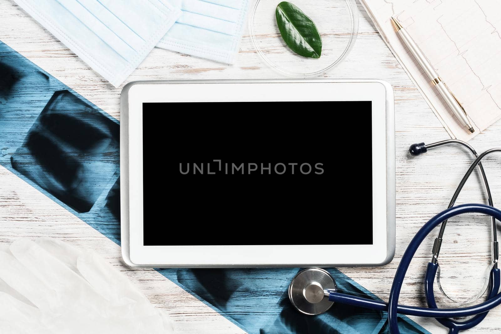 Laboratory result of patient examination lies on doctor table. Top view tablet computer with blank screen, x-ray image, stethoscope and cardiogram on wooden desk. Digital technology in cardiology.