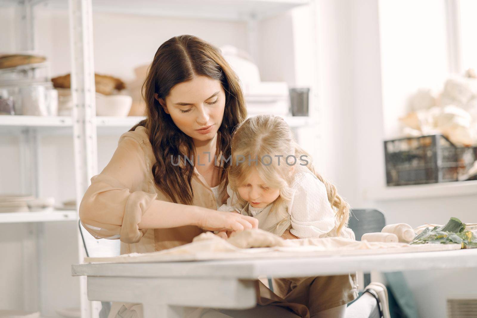 Woman and girl kneading clay. Family make art product at table in pottery workshop. Mother with daughter.