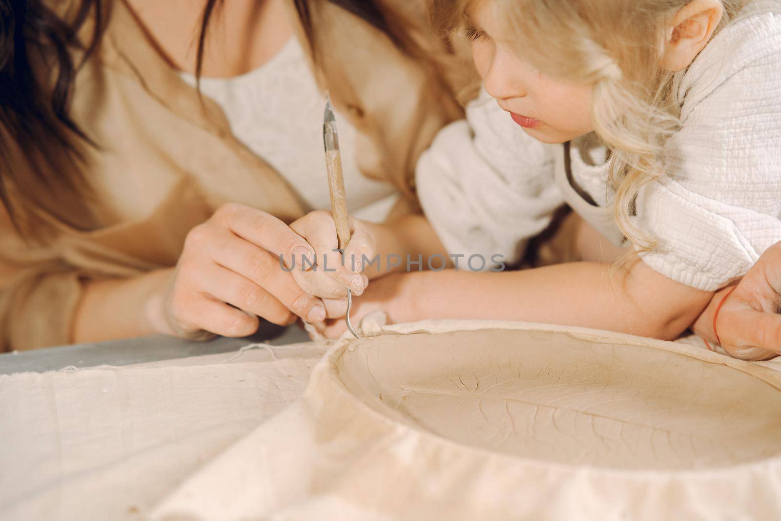 Woman and girl kneading clay. Family make art product at table in pottery workshop. Mother with daughter.