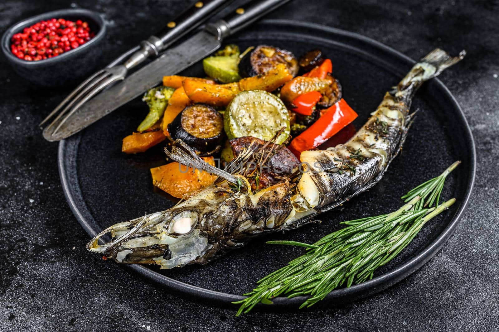 Baked whole icefish with grilled vegetables. Black background. Top view by Composter