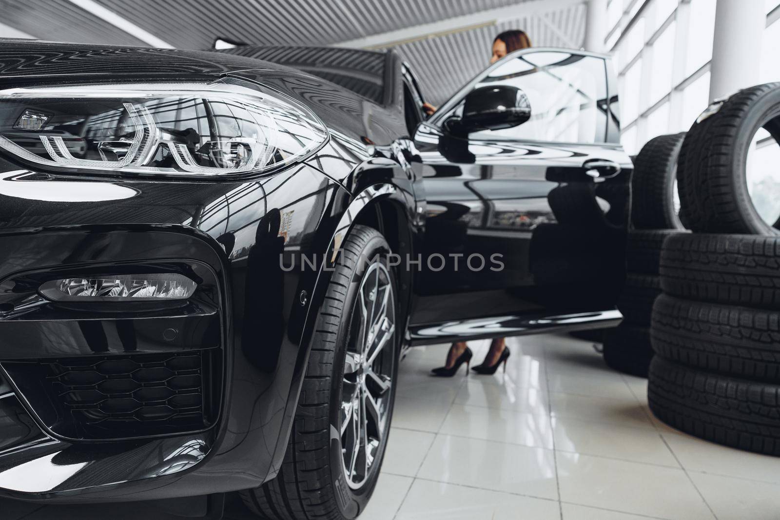 Woman buyer sits down n a black car in car showroom