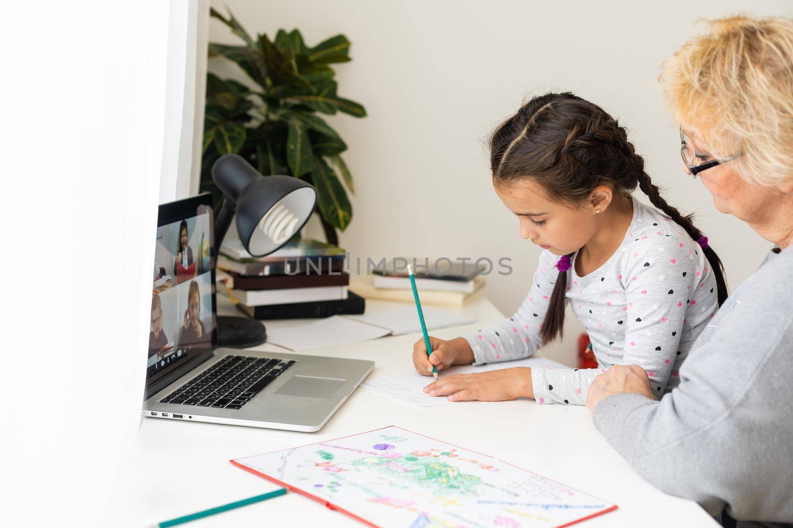 Cute and happy little girl child using laptop computer with her grandma, studying through online e-learning system.