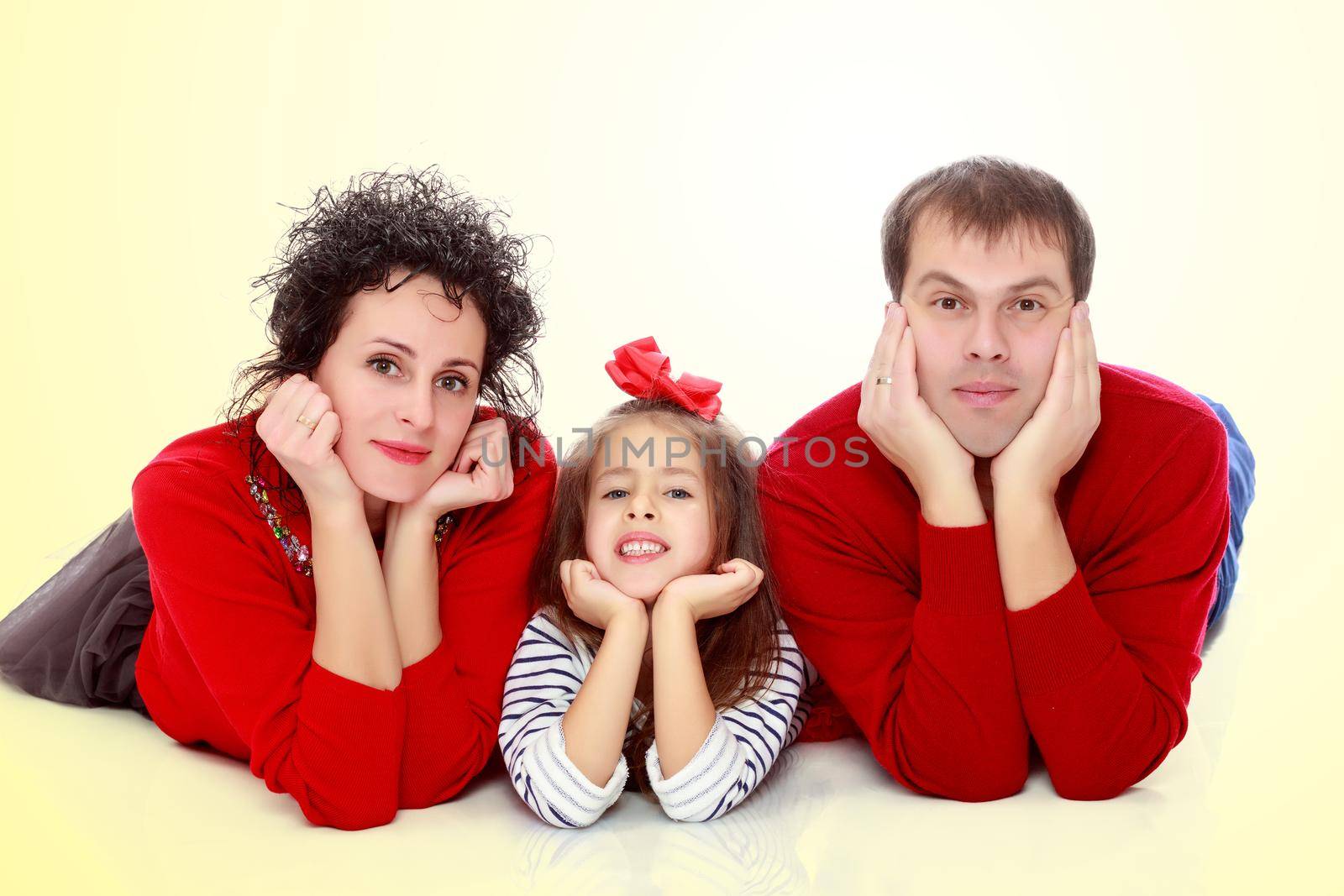 Happy young family dad mom and a little girl in bright red outfits . Family lying on the floor leaning on his hands.