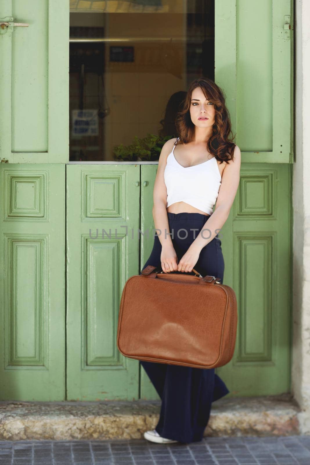Beautiful girl with vintage bag against green door in urban background. Casual spring clothes