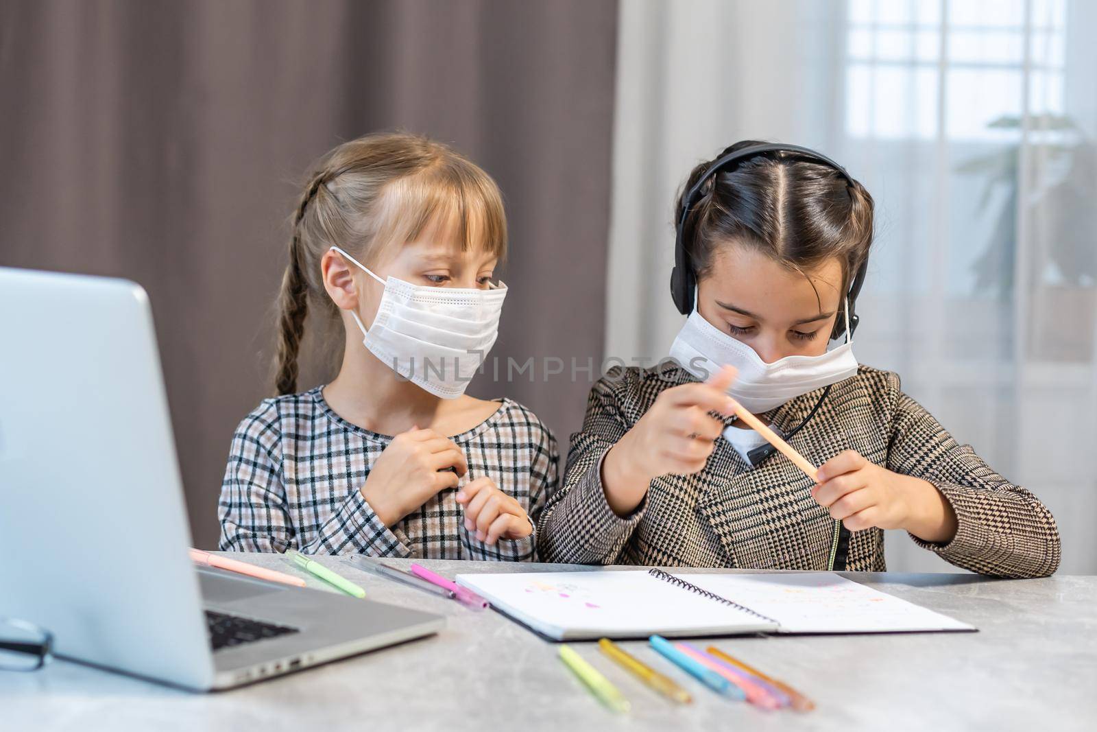 Young elementary school girls with face protective mask watching online education class. Coronavirus or Covid-19 lockdown education concept.
