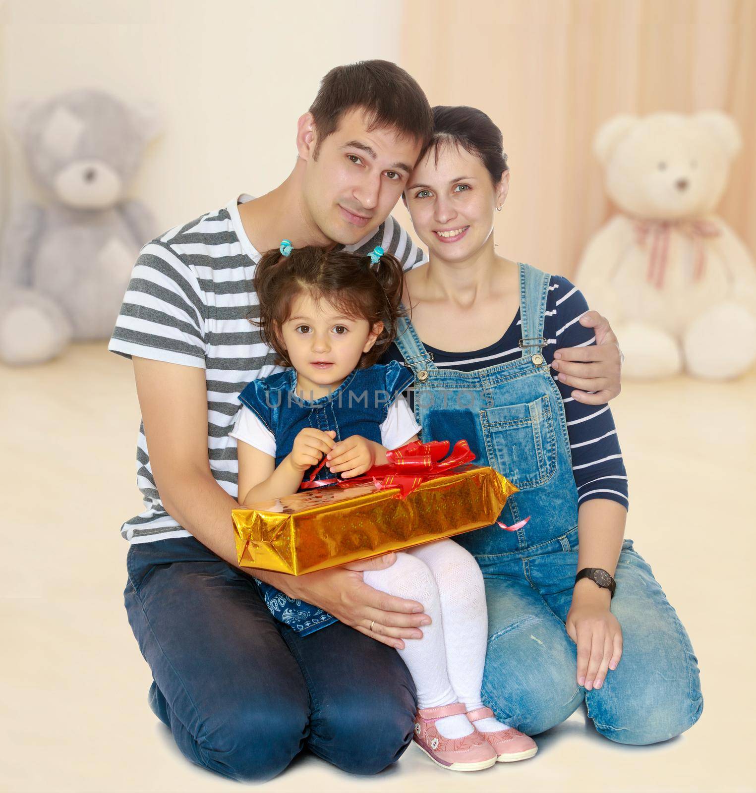 Happy young family with little daughter cuddling together in celebration of Christmas.In the children's room in which sits a Teddy bear.
