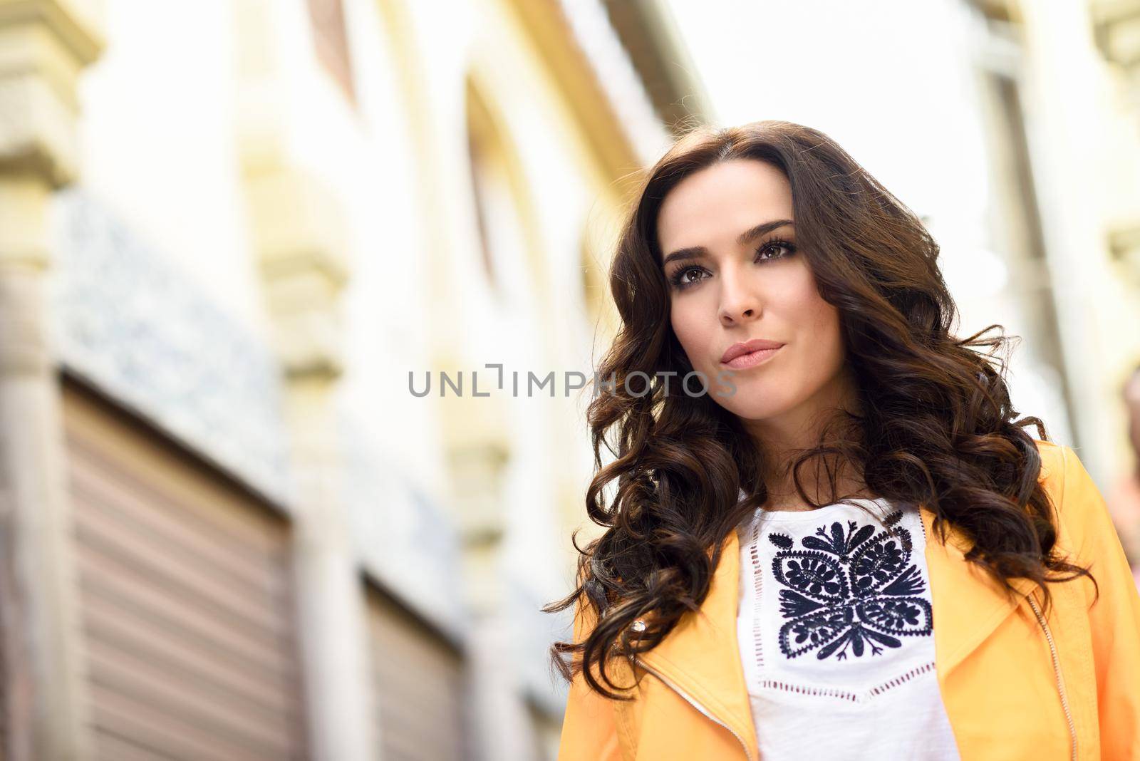 Young brunette woman, model of fashion, wearing orange modern jacket in urban background.