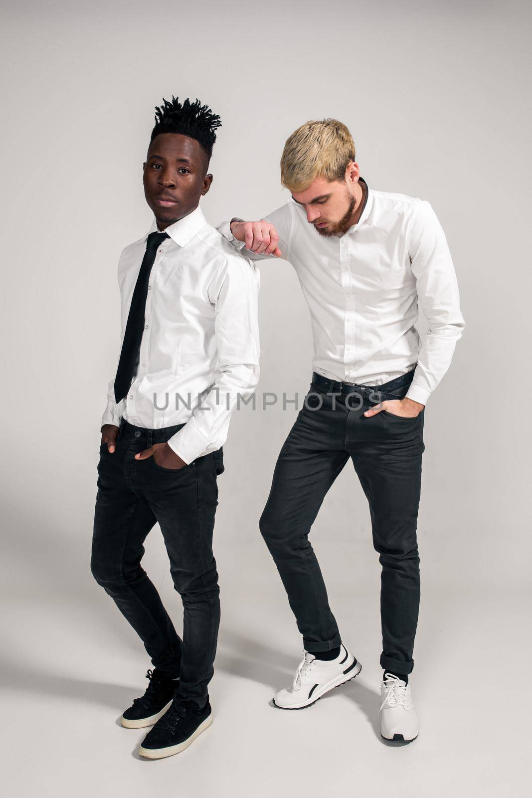 Friends. Two guys in white shirts and dark pants posing in the studio on a white background. Copy space. Full-length photo