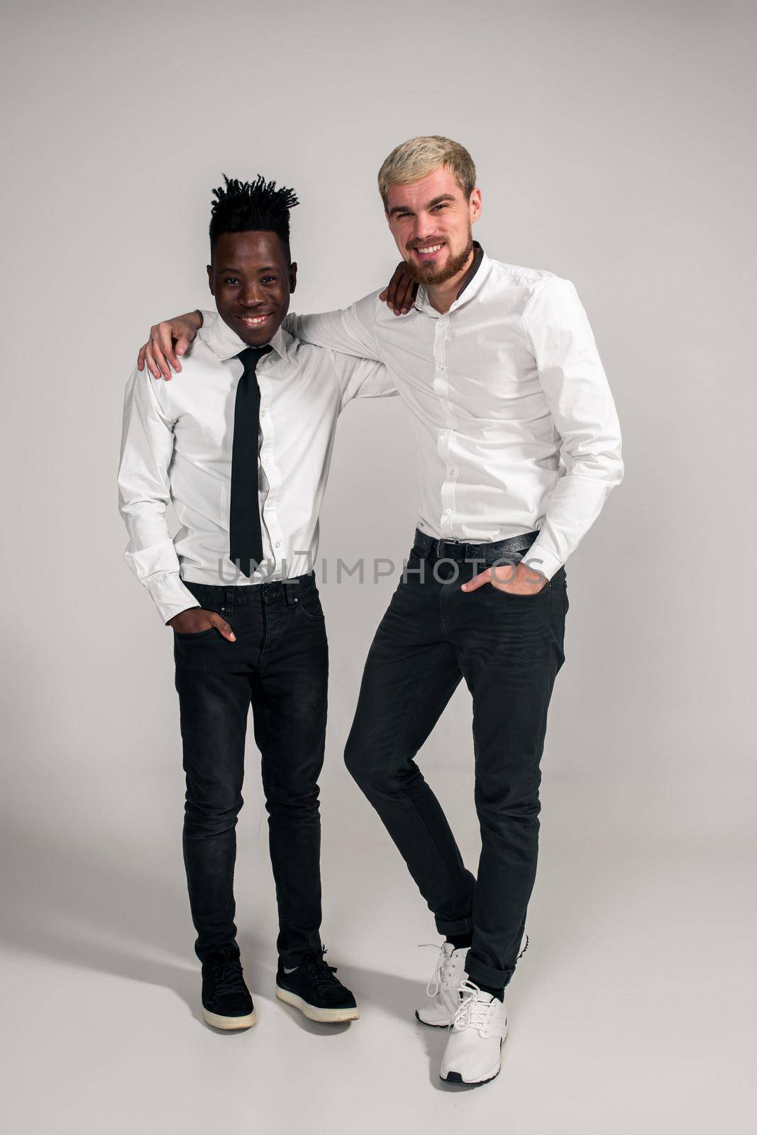 Joyful relaxed african and caucasian boys in white and black office clothes laughing and posing at white studio background with copy space by nazarovsergey