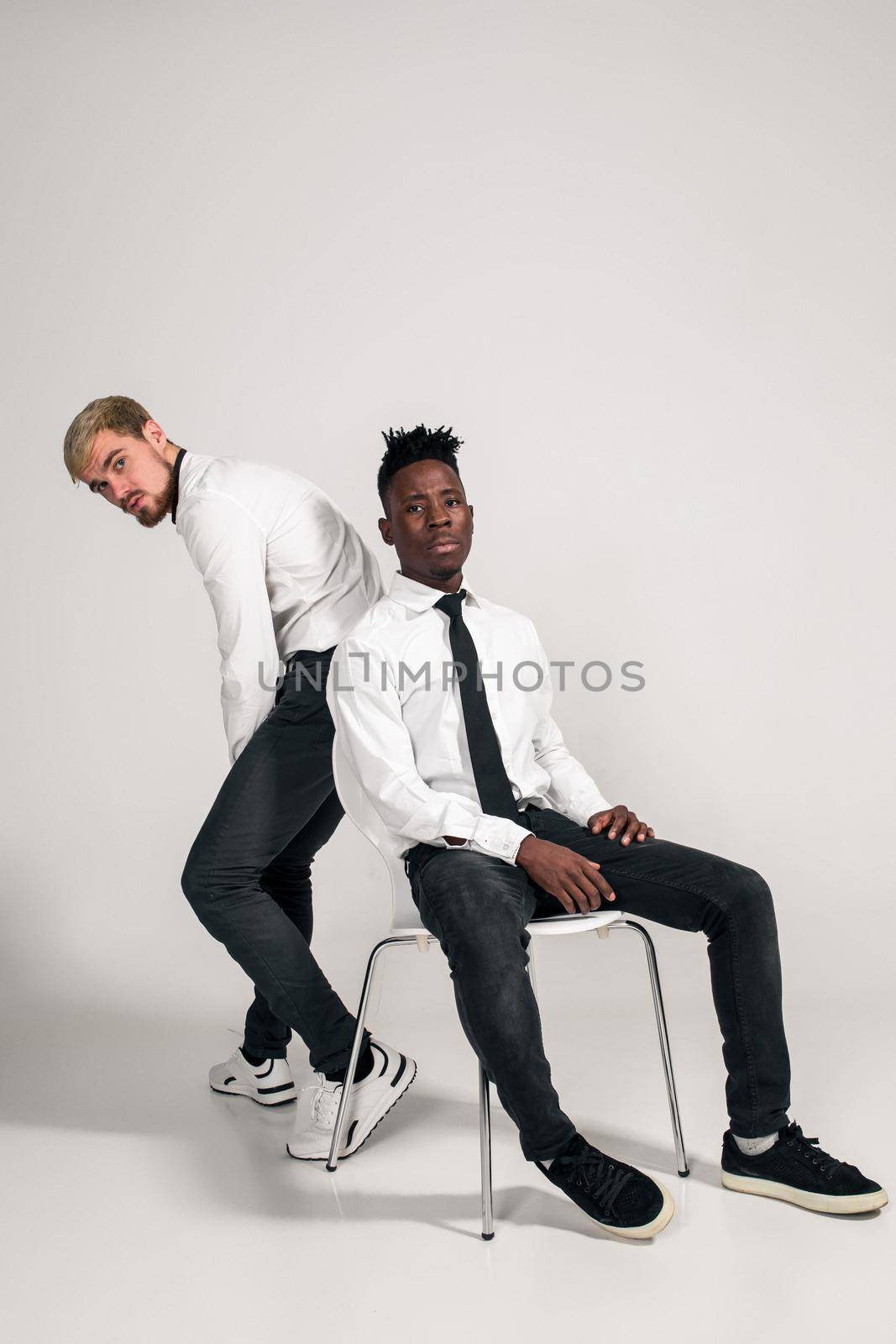 Two stylish men posing and having fun on white background. Friends. Two guys in white shirts and dark pants at studio