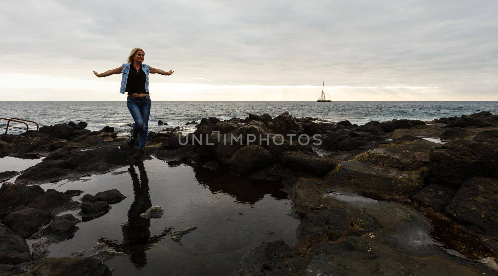 Women on volcanic rocks and blue ocean with waves, white foam and volcanic rocks. Canary Islands. The magnificent coast of the Atlantic Ocean.