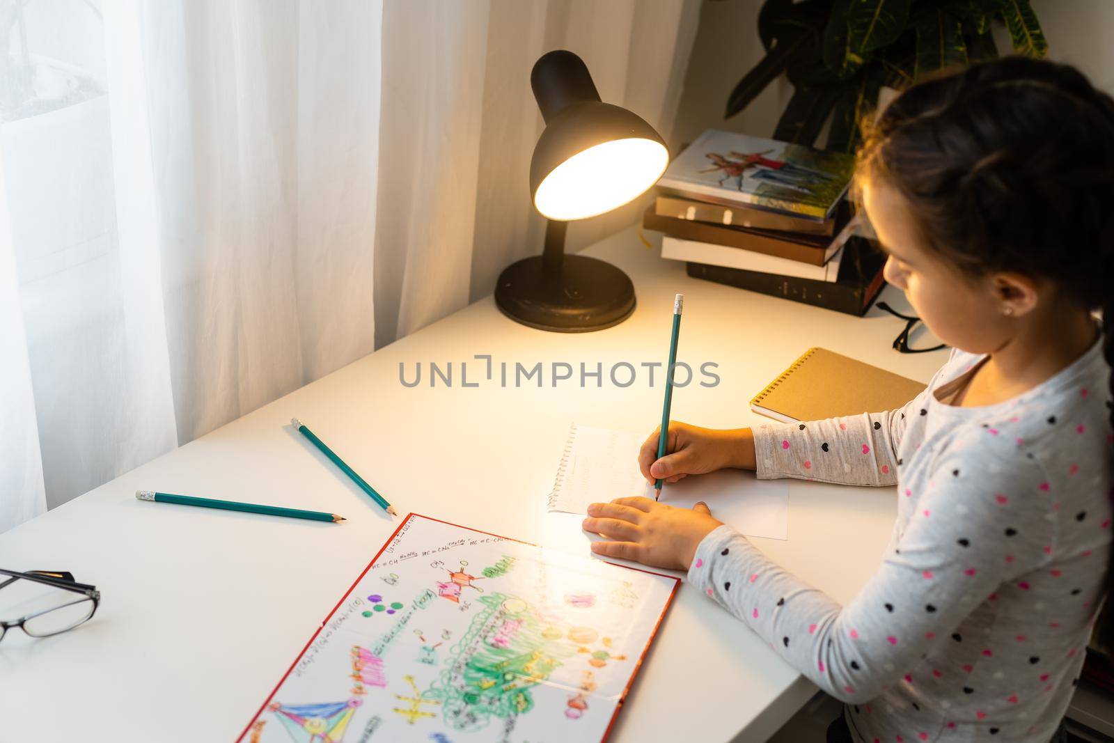 children, education and learning concept - student girl with book writing to notebook at home by Andelov13