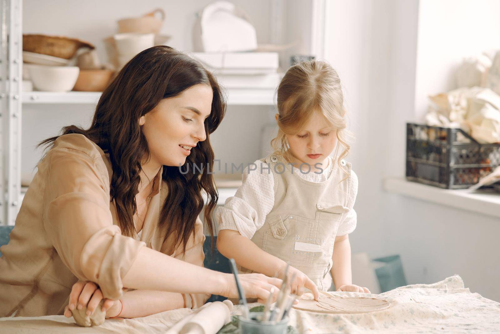 Woman and girl kneading clay. Family make art product at table in pottery workshop. Mother with daughter.