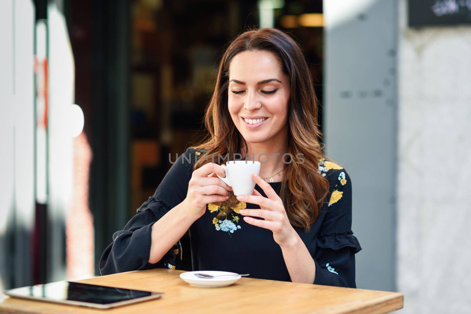 Beautiful woman drinking coffee in an urban cafe bar. Young female sitting at table at an outside terrace. Girl with california highlights hairstyle.