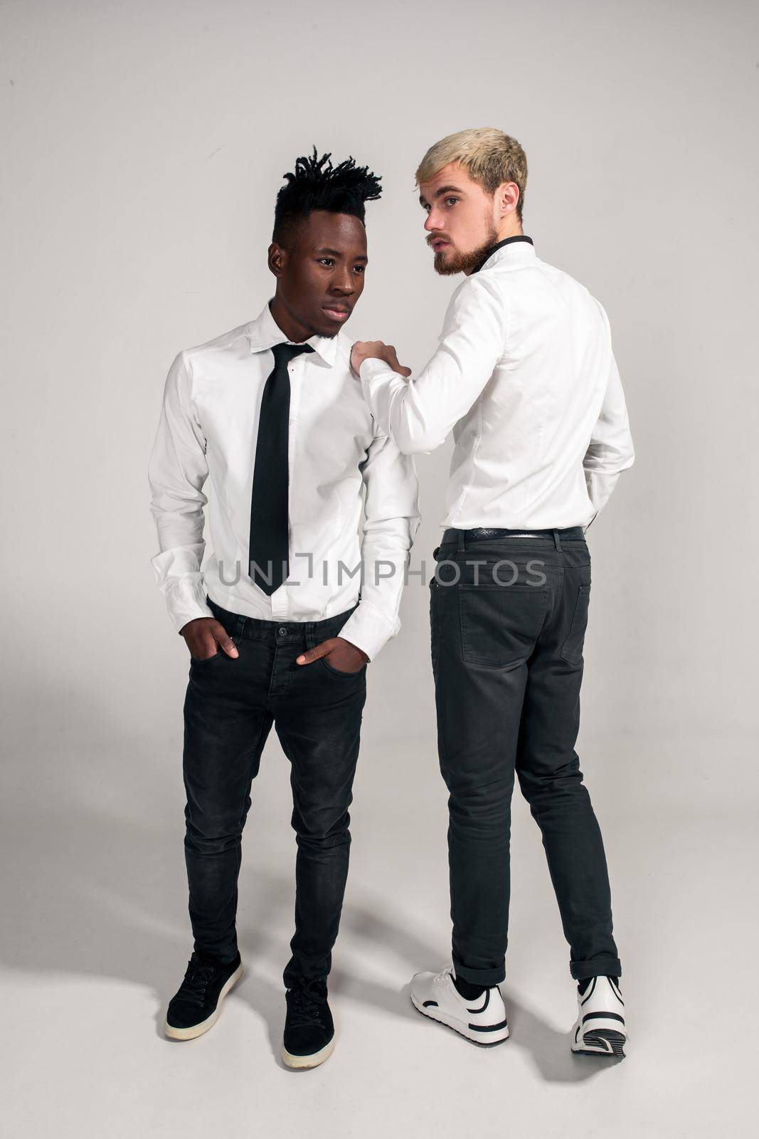 Joyful relaxed african and caucasian boys in white and black office clothes laughing and posing at white studio background with copy space by nazarovsergey