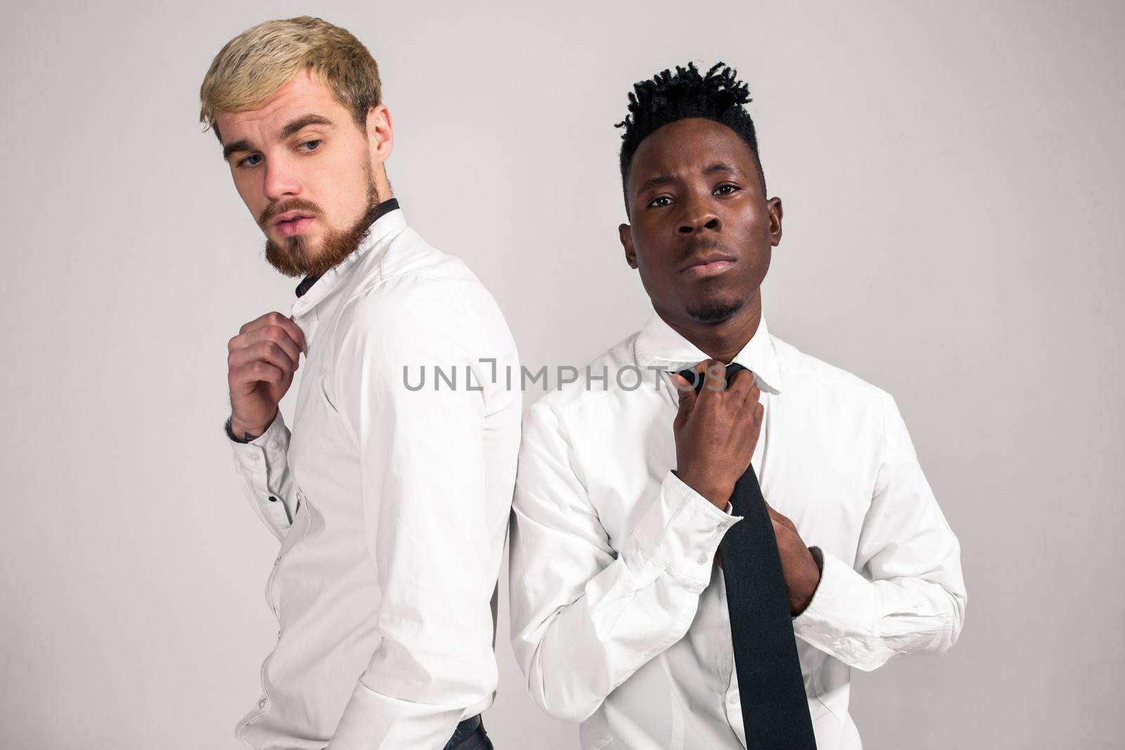 International friendship concept. Studio shot of two stylish young men: handsome bearded young man in white shirt and jeans standing next to his African-American friend on white background