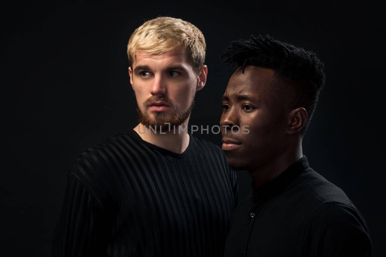 Portrait of two young african american and caucasian men standing over black background. International friendship concept. Studio shot