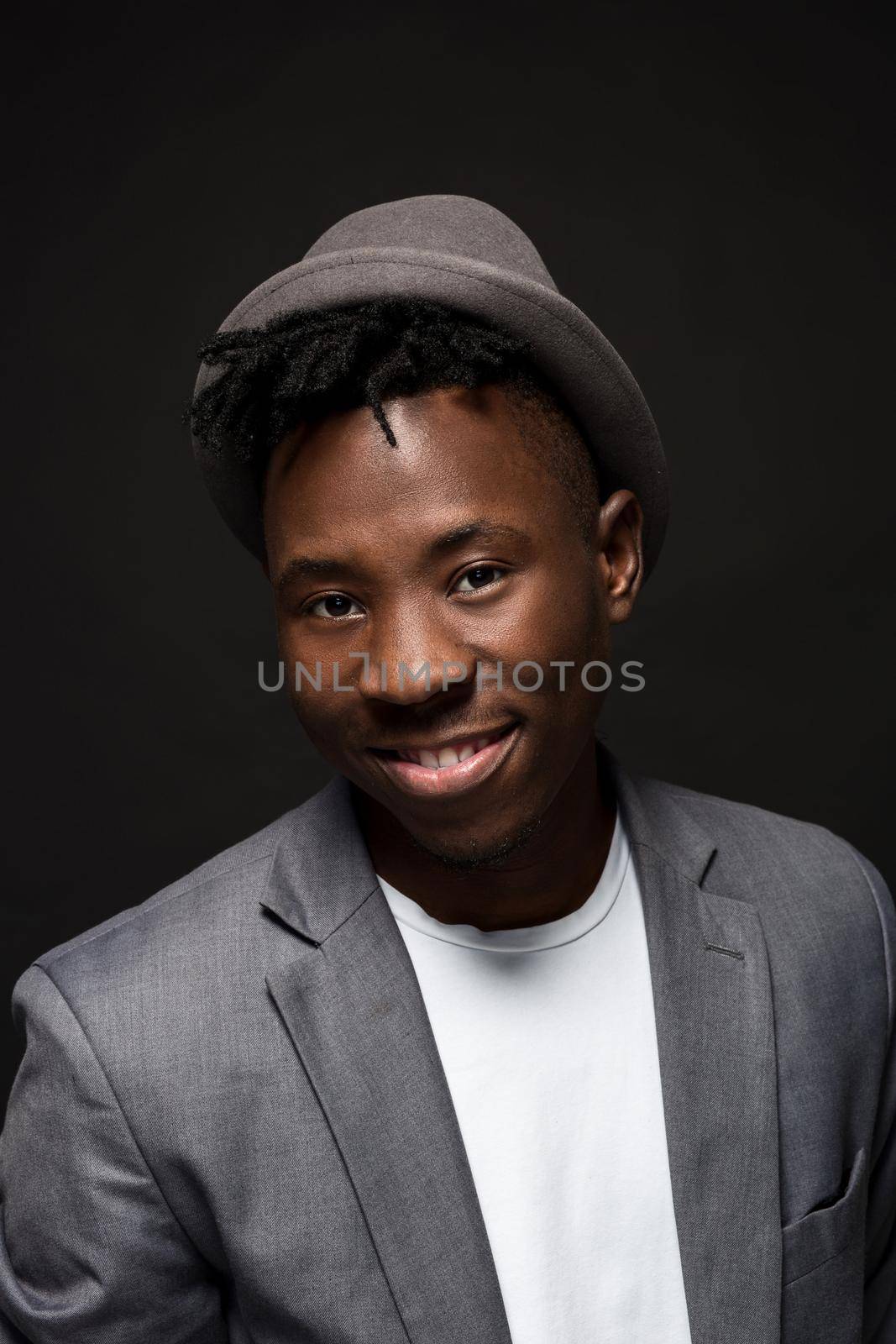 Portrait of attractive young black male studio with hat cheesy smile on dark background. Studio shot
