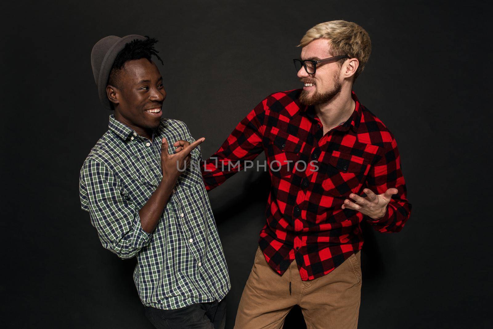 A Friend portraits shot against dark background. Two best friends are posing and having fun in the studio. Dressed in casual clothes, shirts in a cage.