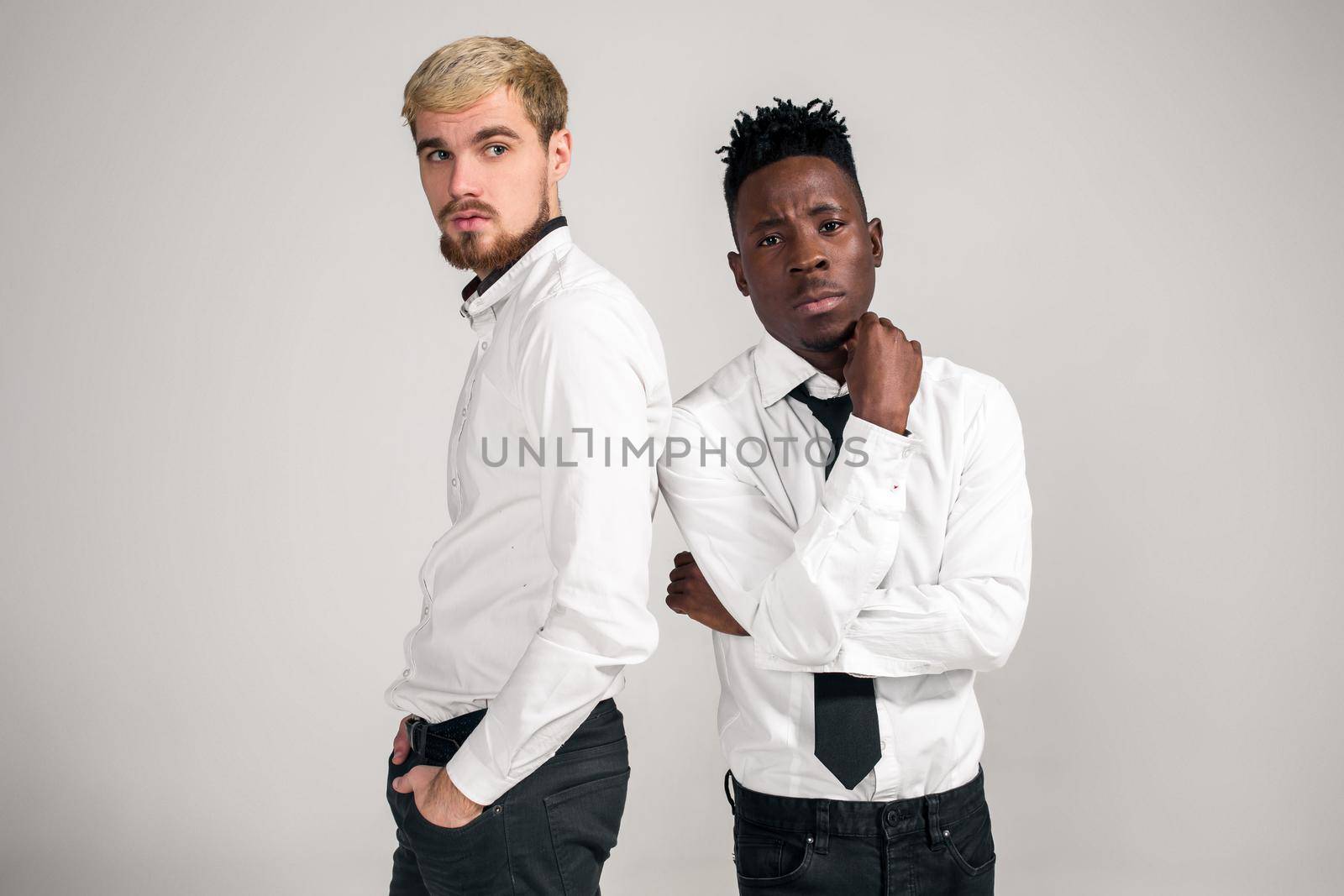 Friends. Two guys in white shirts and dark pants posing in the studio on a white background. Copy space. Belt portrait