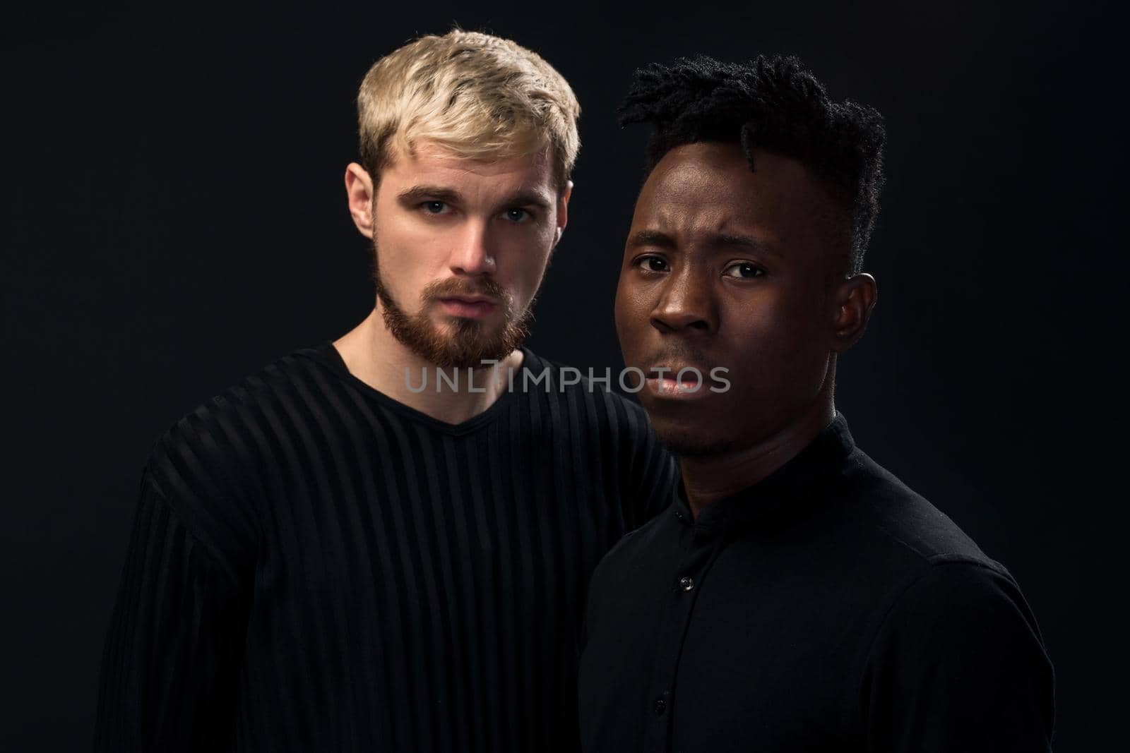 Portrait of two young african american and caucasian men standing over black background. International friendship concept. Studio shot