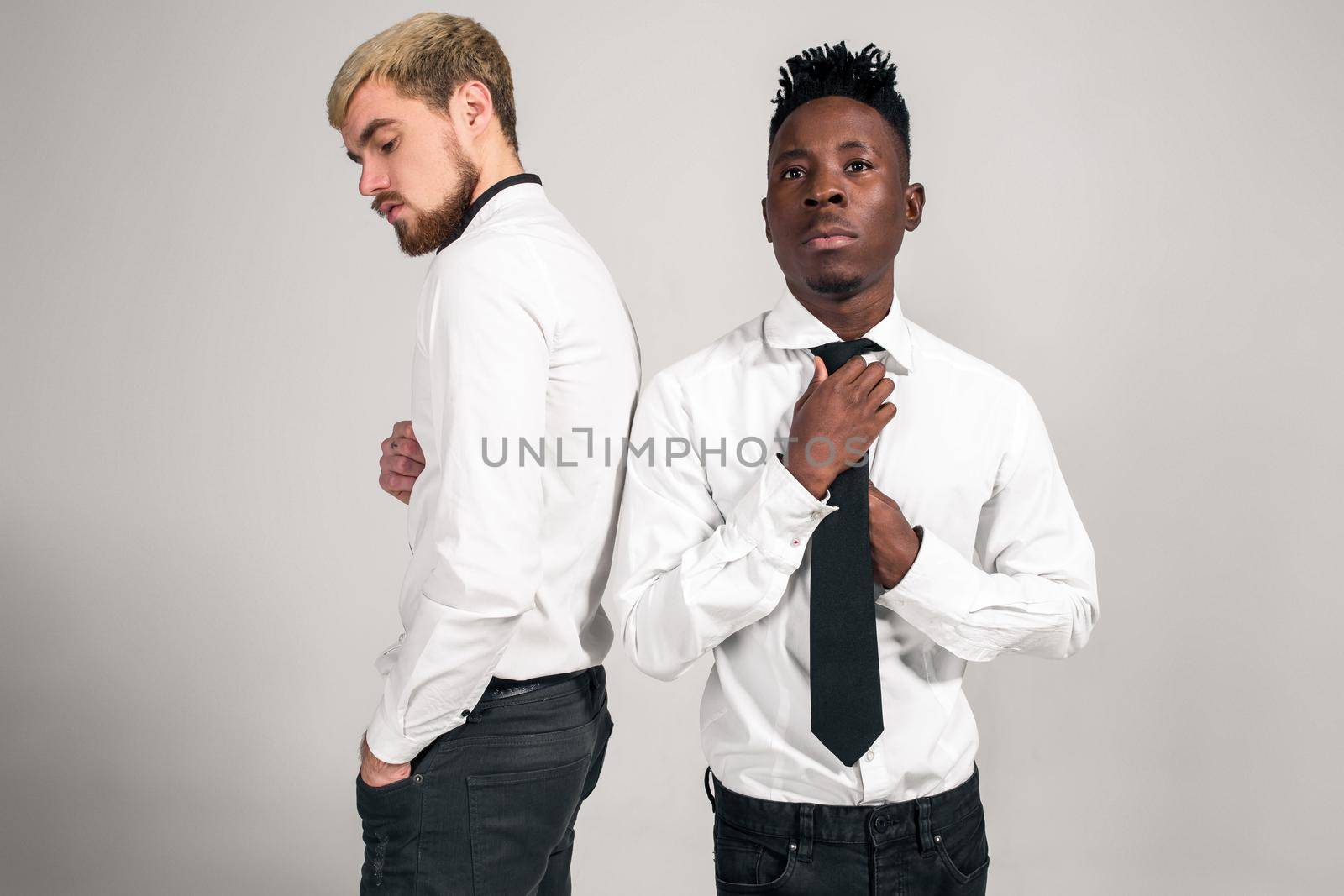 Friends. Two guys in white shirts and dark pants posing in the studio on a white background. Copy space. Belt portrait