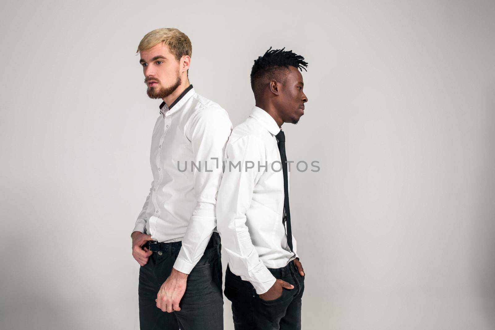 Friends. Two guys in white shirts and dark pants posing in the studio on a white background. Copy space. Belt portrait
