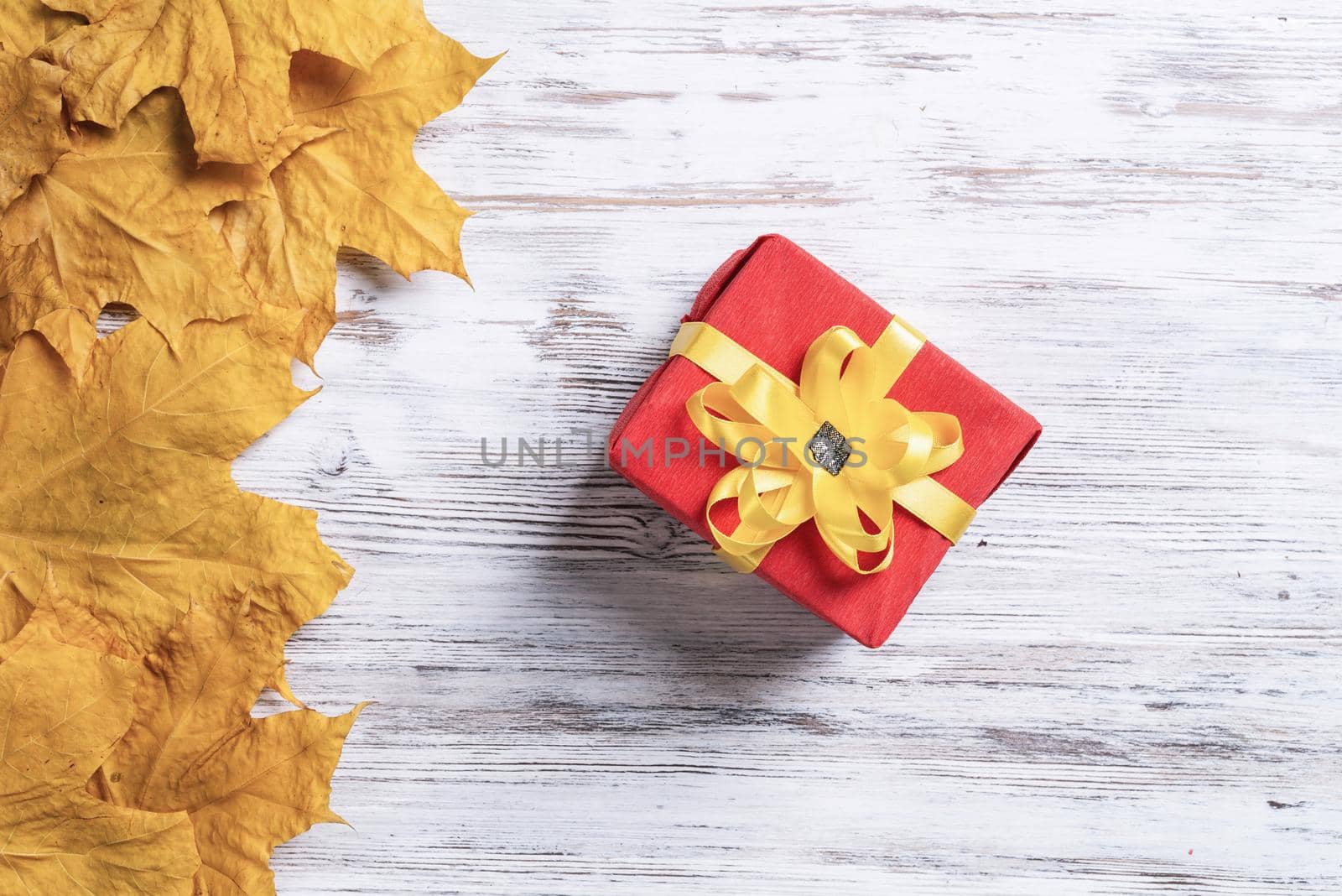 Bright autumn composition with gift box and yellow maple leaves. Holiday present decorated yellow ribbon bow lies on vintage wooden desk. Happy thanksgiving congratulation. Autumn sale advertising.