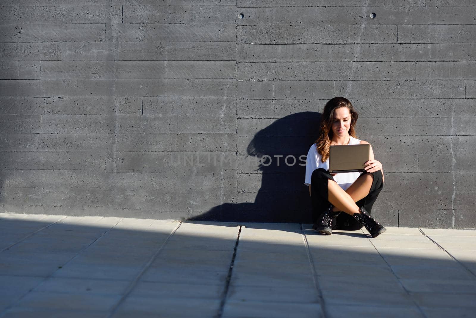 Young businesswoman working with her laptop computer sitting on the floor outdoors.