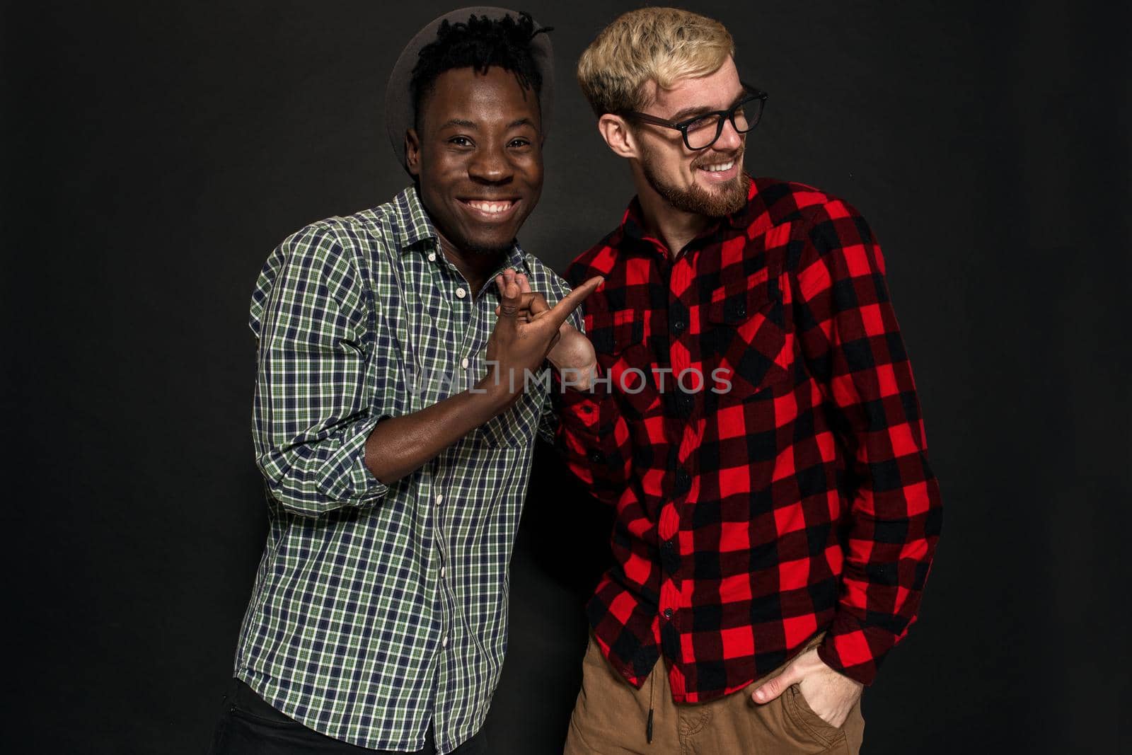 A Friend portraits shot against dark background. Two best friends are posing and having fun in the studio. Dressed in casual clothes, shirts in a cage.