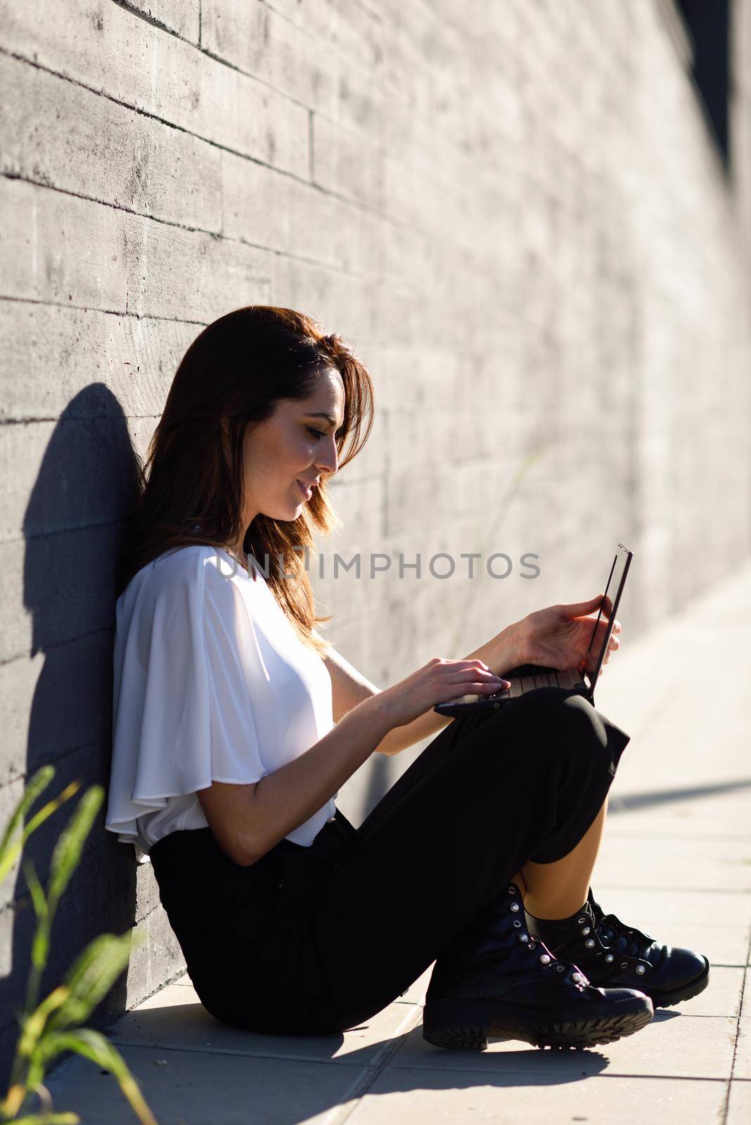 Middle-age businesswoman working with her laptop computer sitting on the floor outdoors.