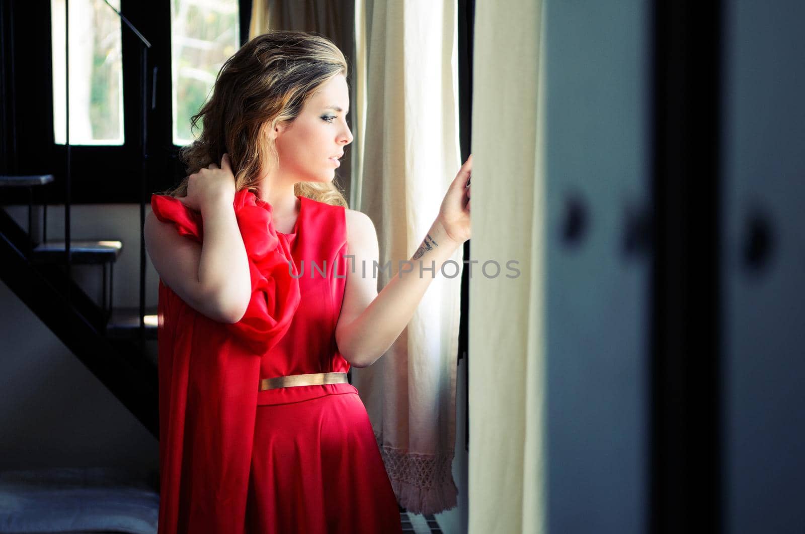 Portrait of a beautiful blonde woman in window wearing a red dress