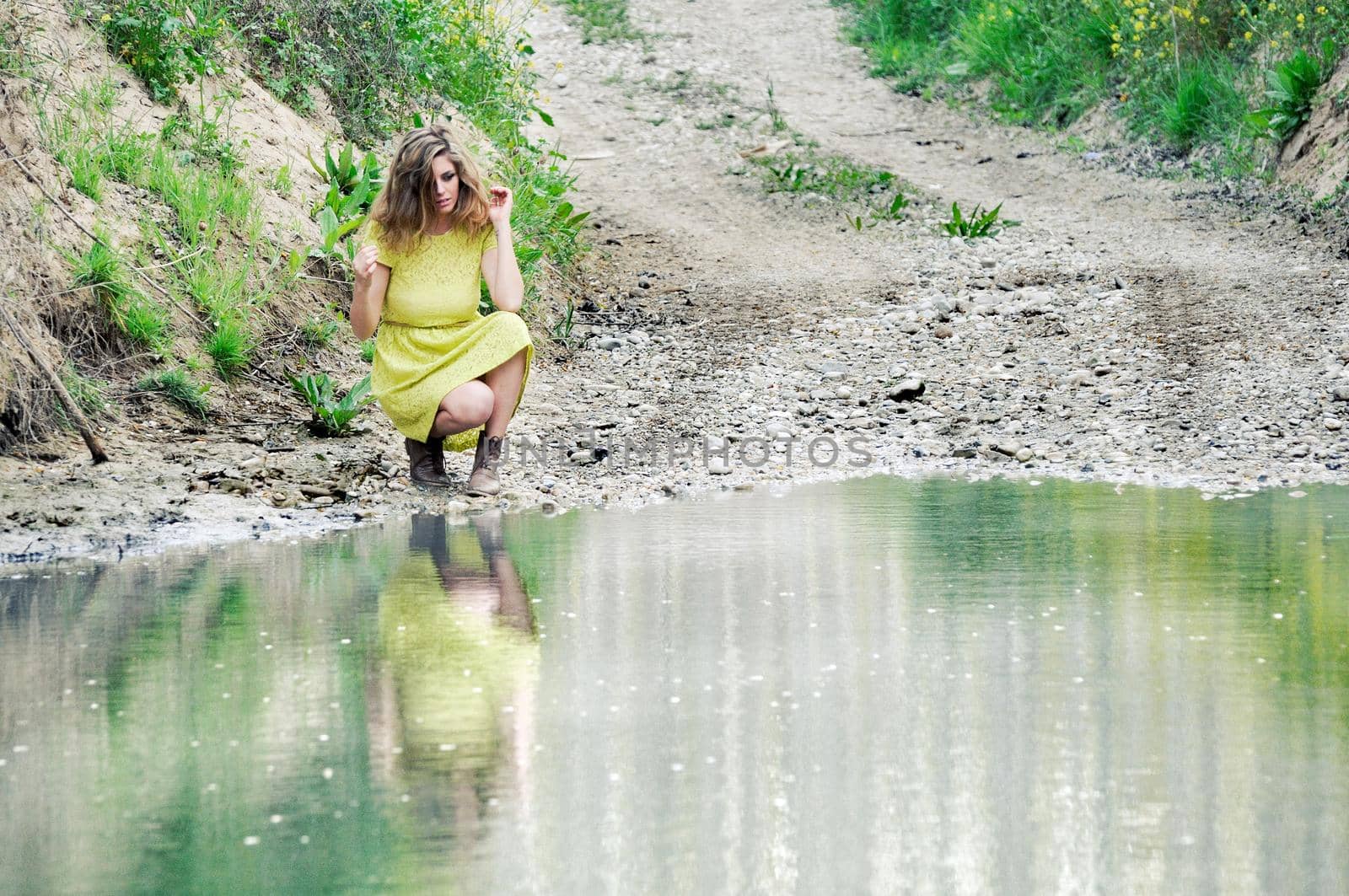 Portrait of a beautiful blonde girl, dressed with a green dress, near a lake