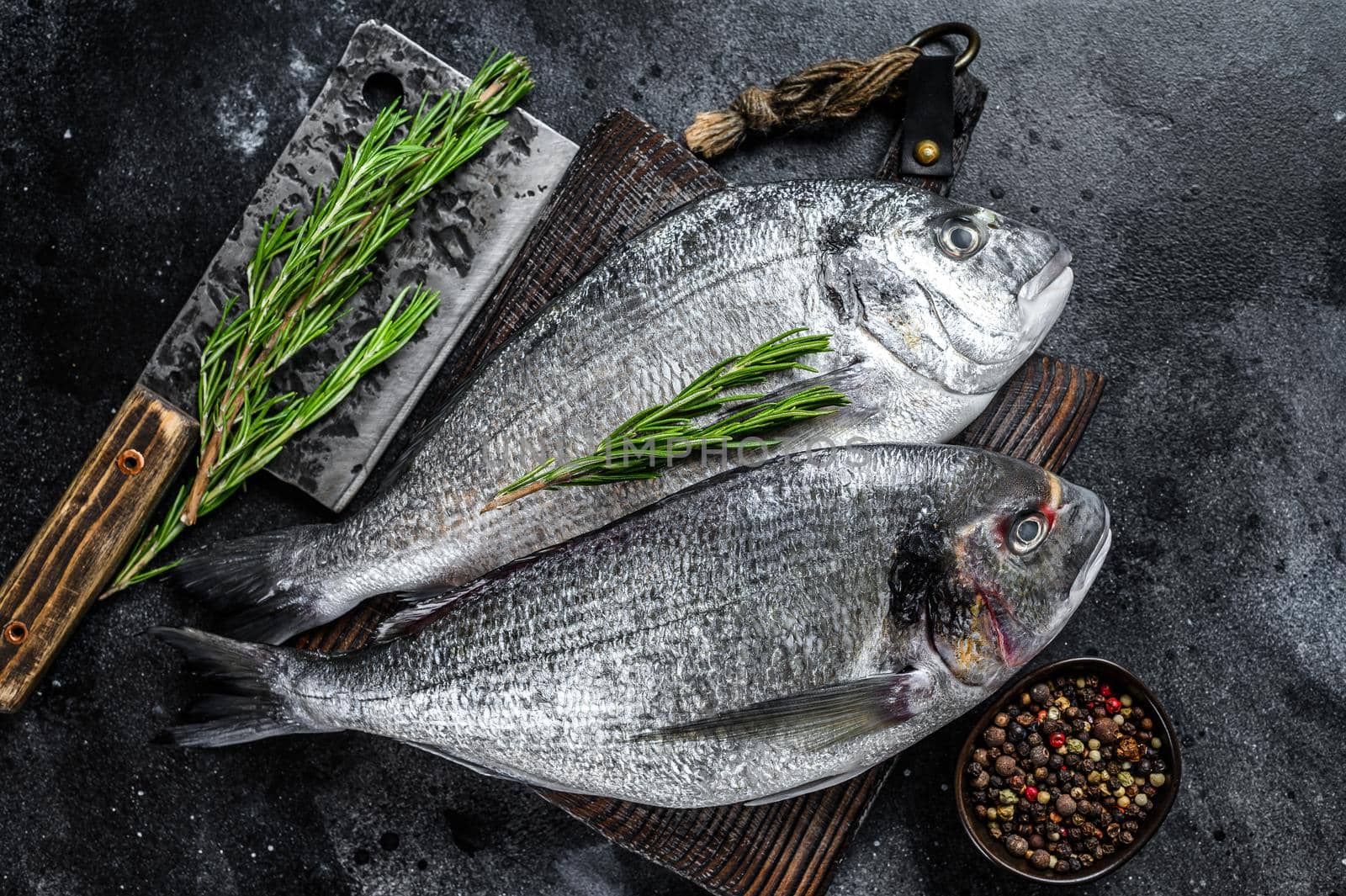 Raw Sea bream dorado fish on a cutting board. Black background. Top view by Composter