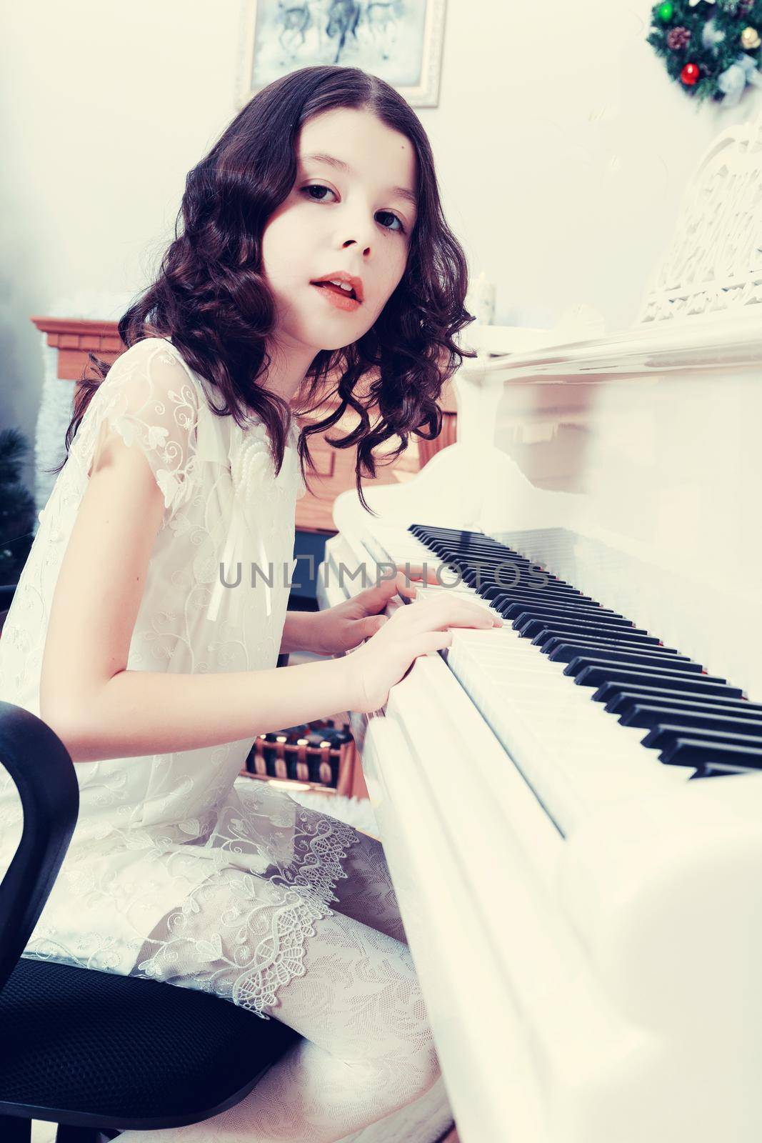 Adorable little girl new year's eve on the backdrop of the Christmas tree plays the piano.Creative toning of a photograph.