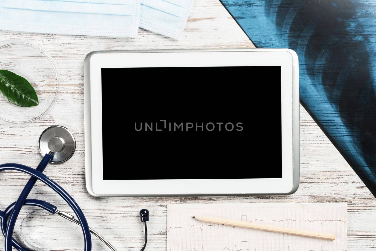 Laboratory result of patient examination lies on doctor table. Top view tablet computer with blank screen, x-ray image, stethoscope and cardiogram on wooden desk. Digital technology in cardiology.