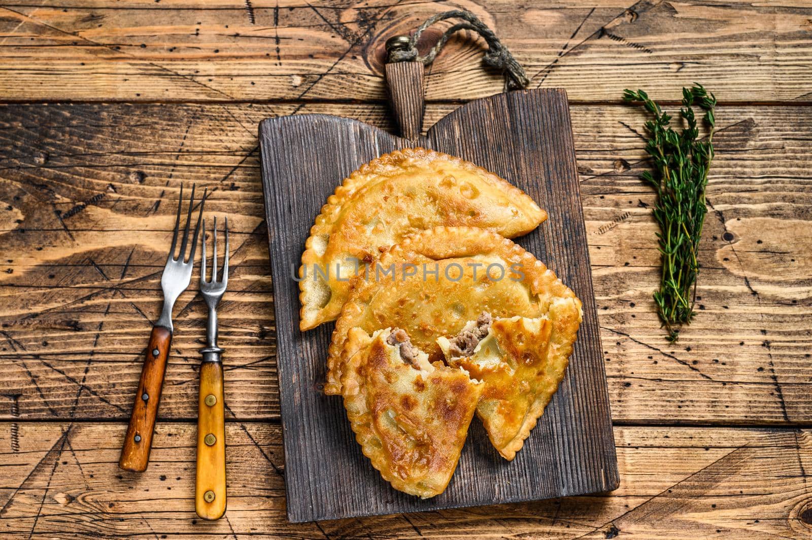 Chilean fried empanadas filled with minced beef meat served on a wooden cutting board. Wooden background. Top view by Composter