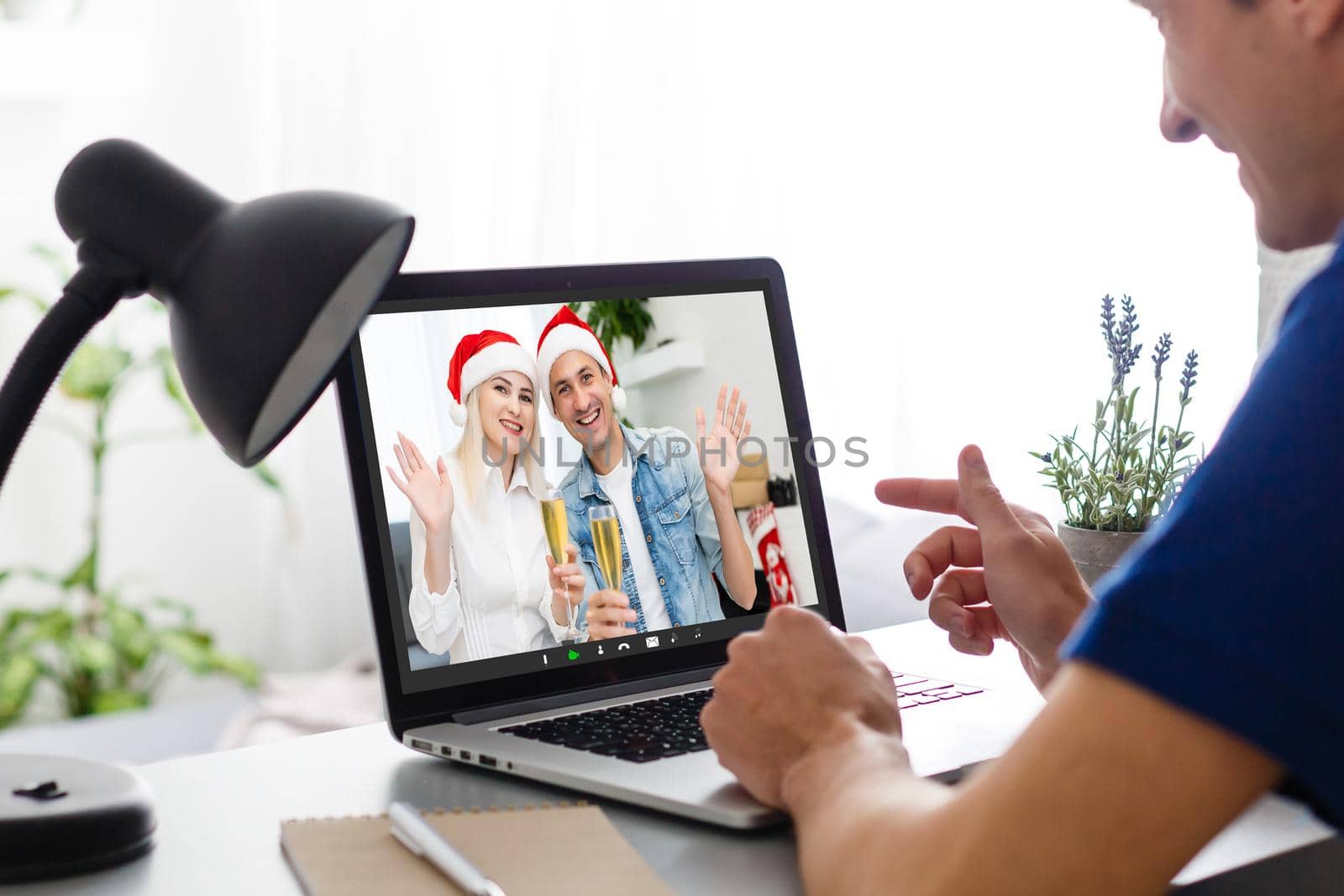 couple waving while having a videocall in santa hats on laptop at home. social distancing during christmas festivity quarantine lockdown concept. by Andelov13