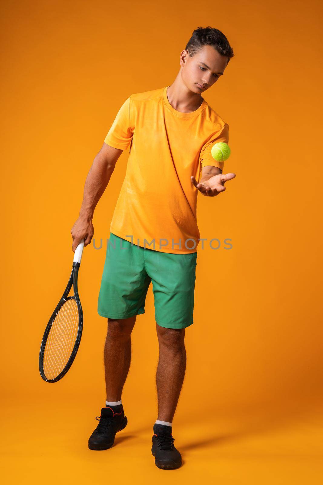 Full-length portrait of a tennis player man in action against orange background close up