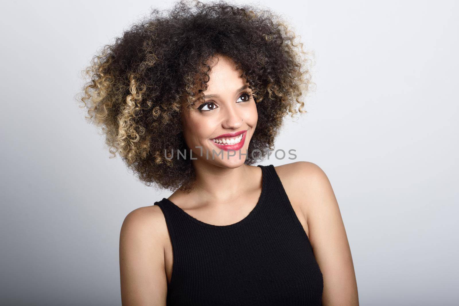 Young black woman with afro hairstyle laughing. Girl wearing black clothes. Studio shot.