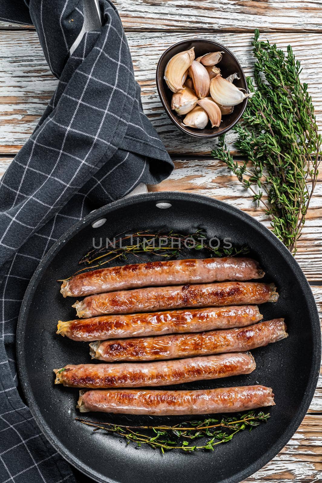 Fried beef and pork meat sausage in a pan with italian herbs and cheese. White wooden background. Top view.