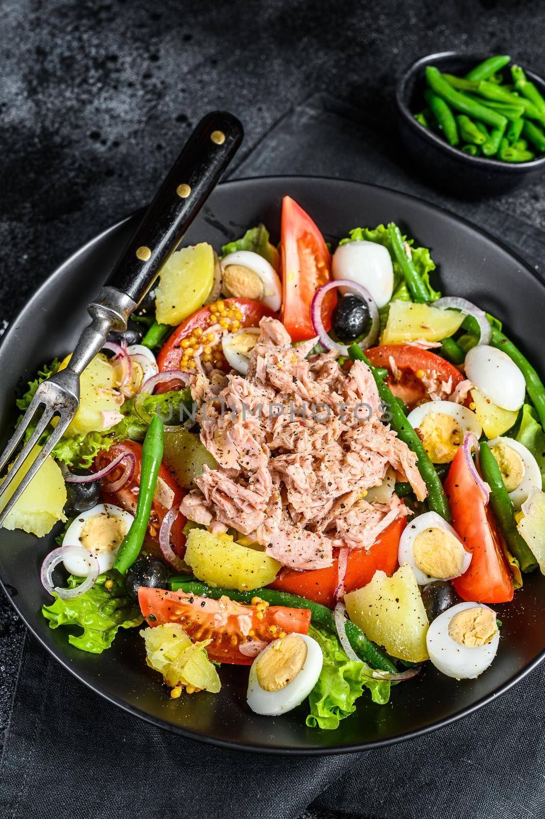 Tuna salad nicoise with vegetables, eggs and anchovies in a plate. Black background. top view.