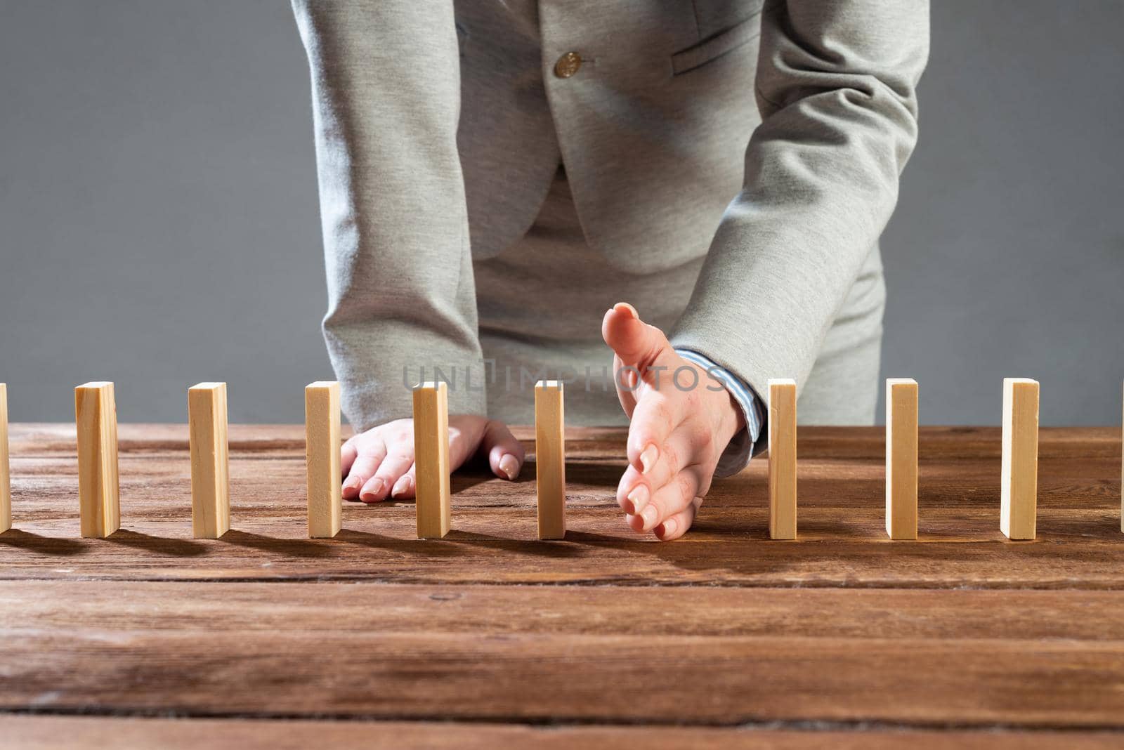 Businesswoman protecting dominoes from falling on wooden desk. Business assistance and leadership in crisis. Operative business solution and stabilization of situation. Professional risk management