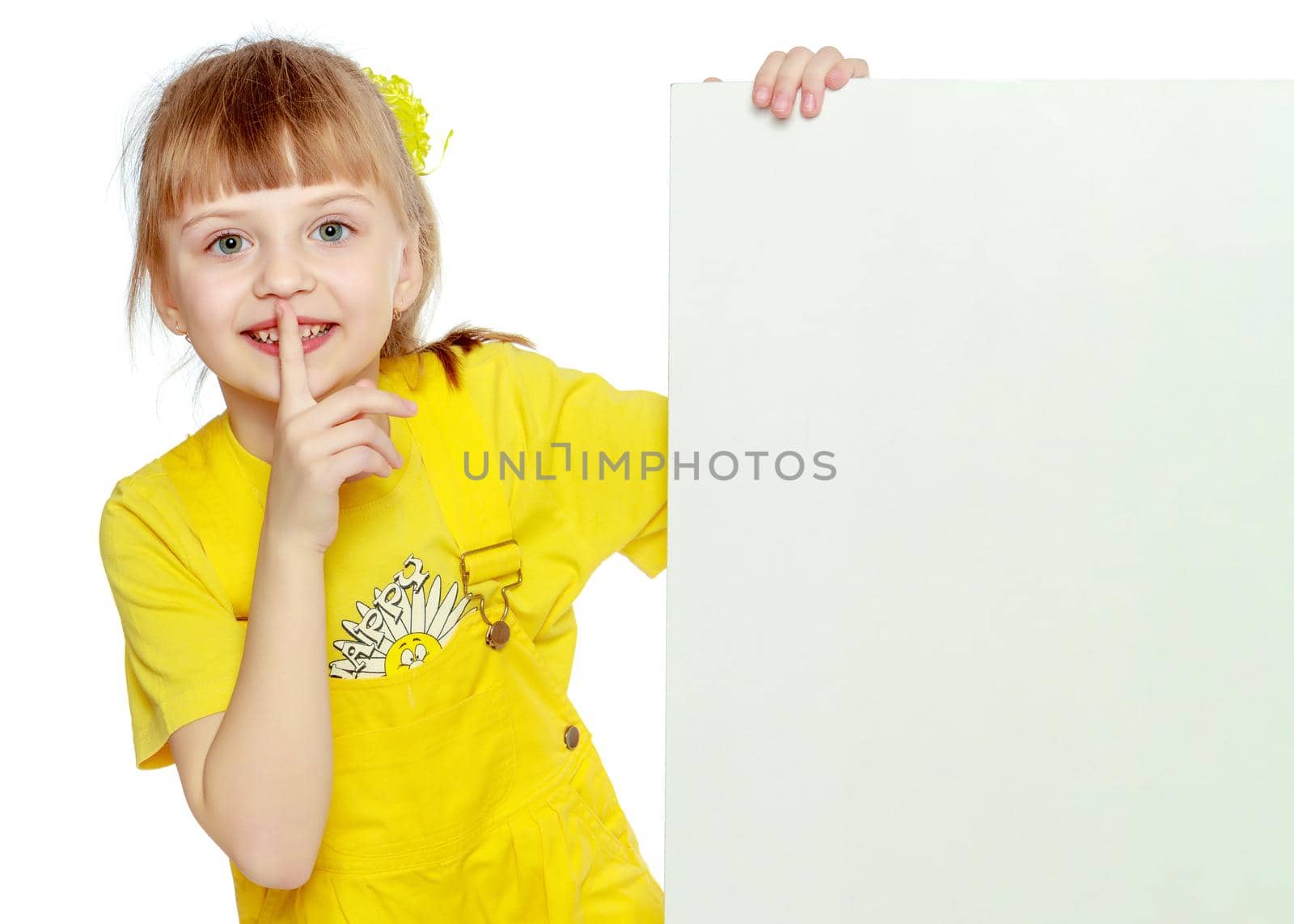 Girl with a short bangs on her head and bright yellow overalls.She crouched down on the white advertising banner.